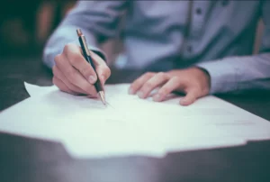 Mains tenant un stylo pour remplir des documents administratifs funéraires.